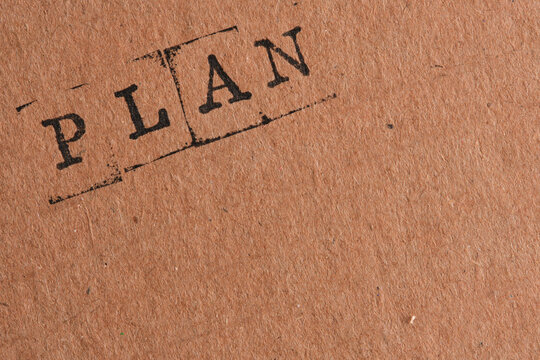 Word PLAN stamped diagonally on brown recycled paper texture, ideal for business concepts.