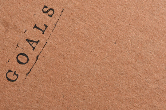 Word GOALS stamped in black retro ink on diagonal kraft paper textured surface background.