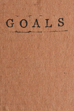 Word GOALS stamped in black ink at top vertical craft paper with empty copy space.