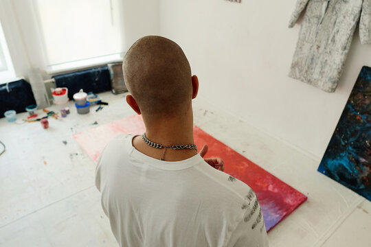 High angle view of young adult artist creating abstract floor painting in studio, expressing contemporary creativity and visual branding. Ideal for art marketing, culture campaigns