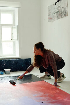 Vertical shot of young adult Caucasian woman creating floor painting in studio, expressing contemporary art practice. Ideal for creative industry marketing, artist branding, gallery promotion