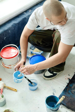 Vertical shot of high angle view of young adult man mixing blue paint in studio, preparing materials for contemporary artwork and creative production. Ideal for artist branding, workshop promotion