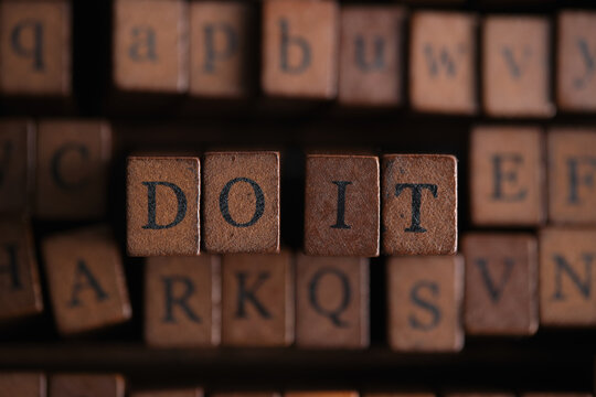 Close up shot phrase DO IT stamped on wooden blocks surrounded by dark vintage typography stamps.