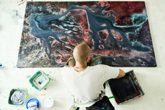 Overhead shot of young adult man creating abstract painting on large canvas in studio, expressing contemporary art practice. Ideal for creative branding, artist promotion, gallery marketing