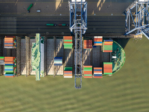 Aerial view of a large container ship being loaded with colorful shipping containers by a massive crane at a port in the United Kingdom.