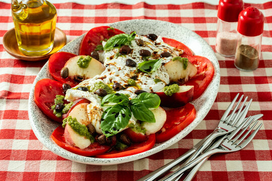 Italian style salad with tomatoes, peaches, olives, burrata and pesto on a set dining table
