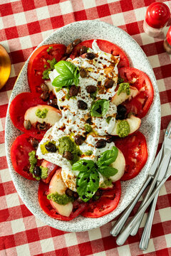 Close up of Italian style salad with tomatoes, peaches, olives, burrata and pesto on a set dining table