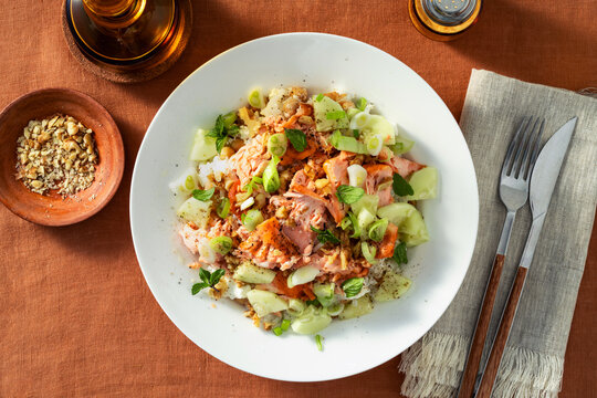 Baked salmon salad with cucumbers, chickpeas, walnuts, feta and rice served on a summer style dining table
