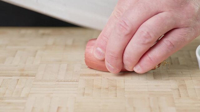 Finely chopping a fresh shallot with a sharp chef knife on a wooden cutting board. Real-time food preparation footage showcasing precise slicing technique and fresh raw ingredients