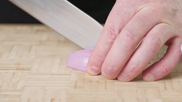 Finely chopping a fresh shallot with a sharp chef knife on a wooden cutting board. Real-time food preparation footage showcasing precise slicing technique and fresh raw ingredients