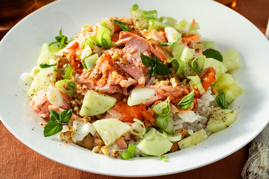 Close up of baked salmon salad with cucumbers, chickpeas, walnuts, feta and rice on a summer style dining table