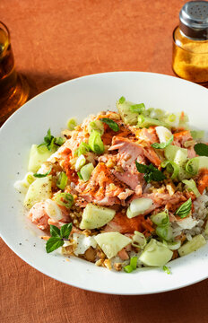 Close up of baked salmon salad with cucumbers, chickpeas, walnuts, feta and rice on a summer style dining table