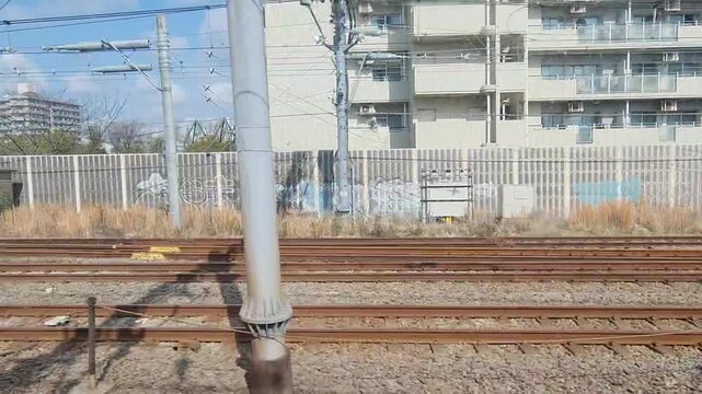 Scenic view of railway tracks and urban infrastructure in Japan captured from a moving train window under a bright sky.