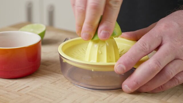 Squeezing a fresh green lime half using a countertop lime/lemon squeezer on a kitchen table. Real-time food preparation footage capturing fresh citrus juice extraction