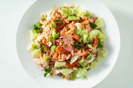 Close up of baked salmon salad with cucumbers, chickpeas, walnuts, feta and rice on white background
