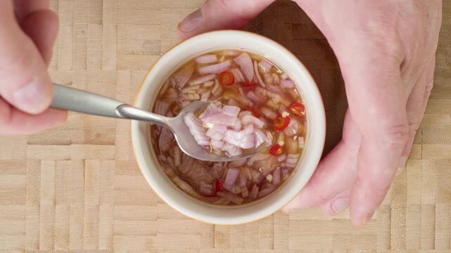 Stirring authentic Thai Prik Nam Pla condiment with a spoon in a bowl. Mixing sliced red chilies, chopped shallot, fresh lime juice, and fish sauce for a traditional spicy Thai dip