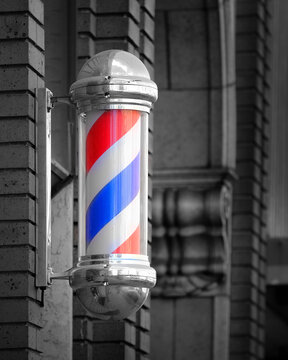 Barber shop sign spinning pole red white and blue on brick wall used to advertise services of Barber Shop