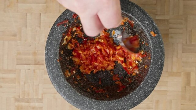 Pounded red chili peppers and fresh garlic cloves in a traditional stone mortar and pestle. Real-time action footage of spooning the aromatic spicy ingredients