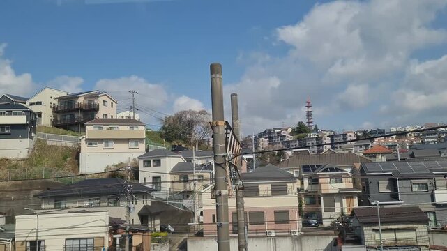 Panoramic view of a densely populated Japanese suburban neighborhood with residential houses and utility poles under a bright blue sky.