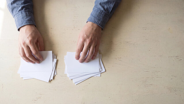 Overhead view of two hands sorting two piles of blank white cards on pale wooden table showing decision making comparison organizing choice and information sorting task concept with copy space