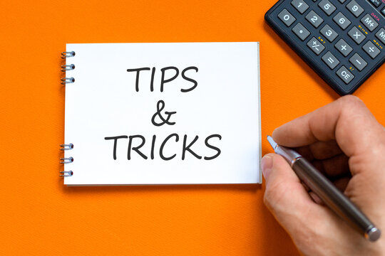 Tips and tricks words symbol. Concept words Tips and tricks on beautiful white note. Beautiful orange background. Businessman hand. Business tips and tricks motivational support concept. Copy space.