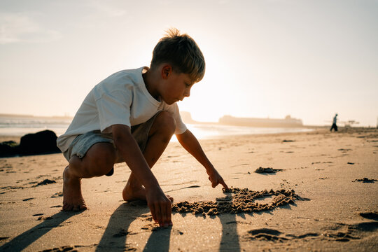 Child Plays in Sand on Beach During Sunset Near the Water
