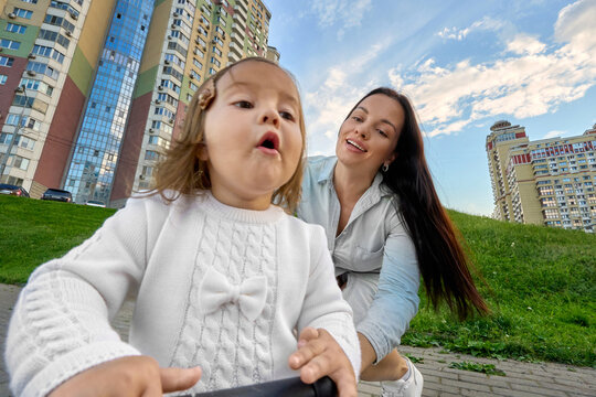 Mother Encouraging Toddler Learning to Ride Balance Bike Outdoors