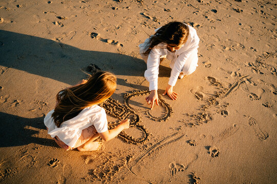 Child and Mother Draw Shapes in Sand on Beach During Afternoon Light