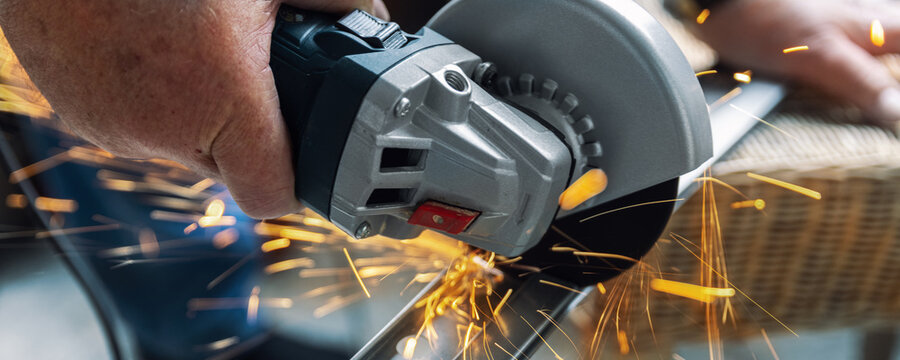 A person is cutting metal with an angle grinder, producing bright orange sparks flying in different directions. The close-up shot captures power, precision and intensity of work
