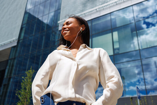 Woman using smartphone with earphones outside office building