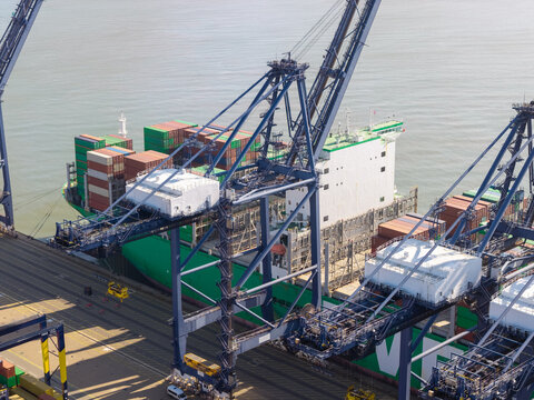 Aerial view of a large container ship docked at a busy shipping port with massive gantry cranes loading cargo containers in the United Kingdom.