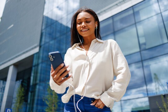 Woman using smartphone with earphones downtown cityscape