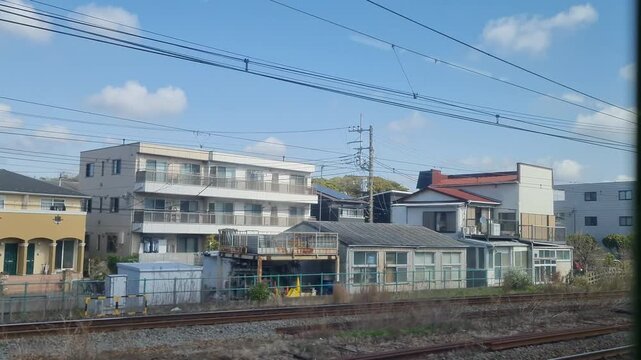 View of railway tracks passing under a blue steel bridge with blooming pink cherry blossom trees and green foliage on a clear sunny day in a suburban transport hub.