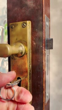 Vertical video social media - Closeup of a man&rsquo;s hand testing two parts to a new security lock just fitted into an old wooden door, by turning the handle for the latch, then the key for the mortice.