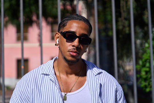 Young man wearing sunglasses, earbuds, and braided hair