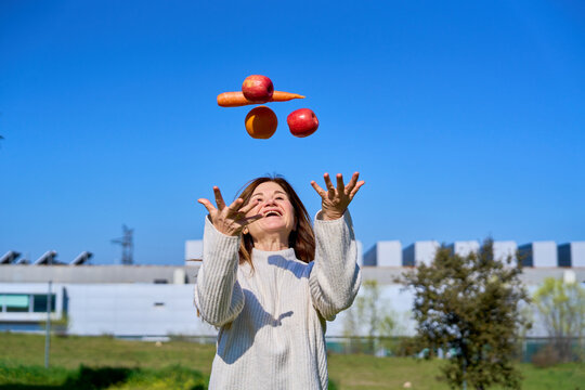 Mature woman juggling fresh fruit, promoting healthy lifestyle