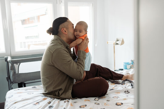 Father kissing baby son in bedroom at home