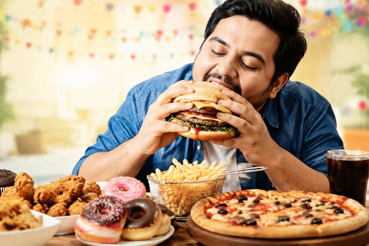 Man with oversized burger and fast food spread, gluttony and excess concept.