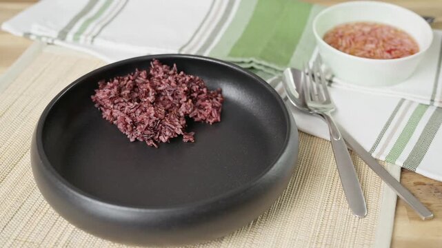 Plating a healthy mixed blend of purple Riceberry and white Jasmine rice into a bowl, prik nam pla on the side.