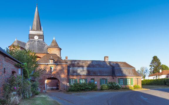Exterior view of Saint-Medard fortified church and traditional red brick buildings in the rural village of Parfondeval in northern France.