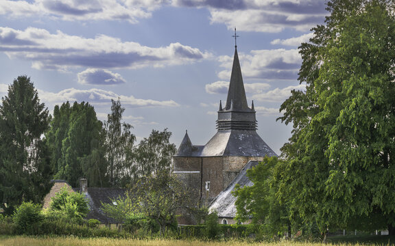 Saint-Medard fortified church with its tall slate spire rising above trees and village houses in Parfondeval, Aisne.