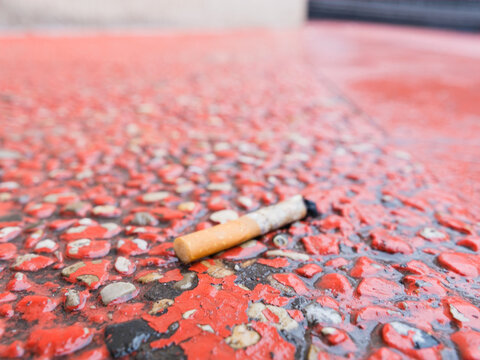 A single discarded cigarette butt rests on a wet red stone pavement