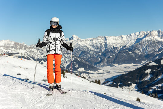 Young adult confident woman skier portrait at winter alpine skiing resort. Female sporty person with backpack mountain Alps snow slope outdoors cold snowy sunny backlit light day