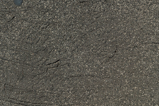 ​Top view horizontal photo of dark textured asphalt pavement on a sidewalk, featuring a rough surface with granular details and small cracks in daylight