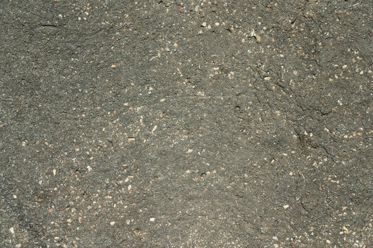 ​Top view horizontal photo of a close up background texture of dark gray asphalt road pavement surface with granular stones and rough detail in daylight