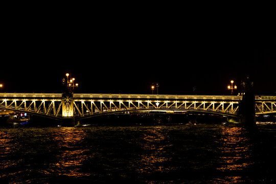 Trinity Bridge in St. Petersburg. Illuminated bridge at night over a river with reflections on the water and streetlights casting a warm glow in the surrounding darkness