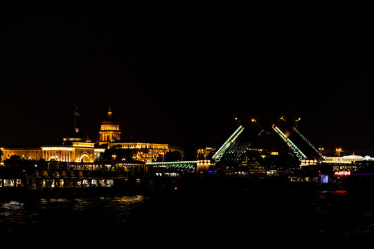 Night view of illuminated cityscape with Dvortsovy (Palace)drawbridges and historic buildings along the Neva riverbank in a vibrant urban setting, St. Petersburg