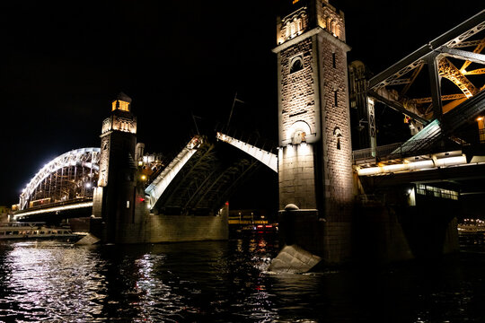 Bolsheokhtinsky Bridge in St. Petersburg. Illuminated bridge over a river at night with reflections on the water and city buildings in the background