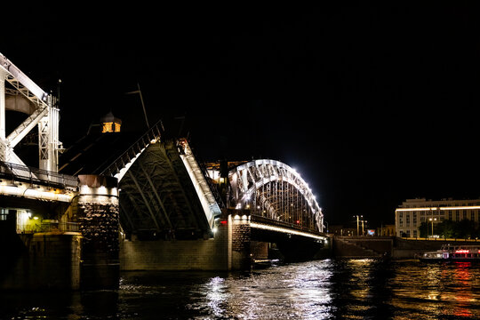 Bolsheokhtinsky Bridge in St. Petersburg. Illuminated bridge over a river at night with reflections on the water and city buildings in the background