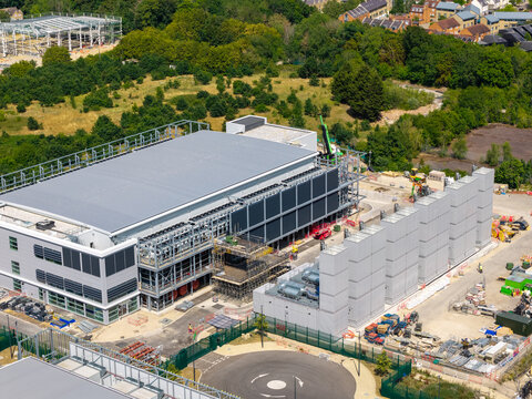 Aerial view of a data center construction site featuring a large industrial building, external cooling units, and construction equipment surrounded by greenery in the United Kingdom.